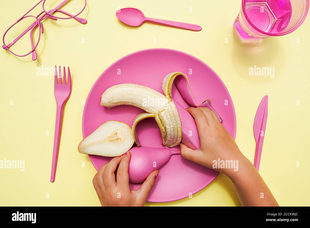 Main de bébé fille de ramasser la poire et la banane de couleur rose de la plaque en plastique Banque D'Images