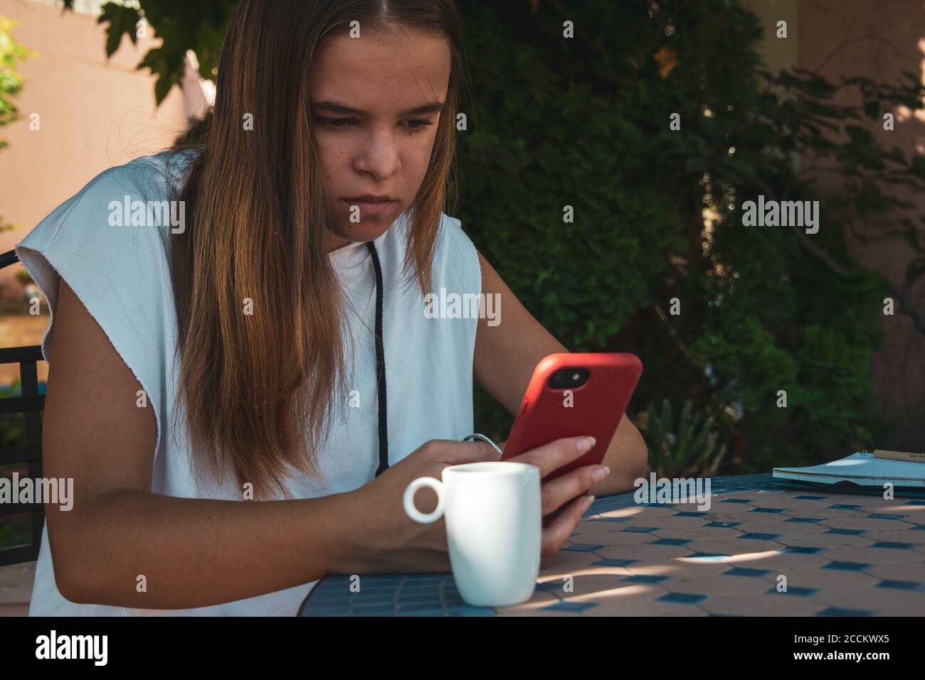 jeune femme dans le jardin avec téléphone mobile, étudier ou se détendre . portant un short et une chemise. , assis à la table. Banque D'Images