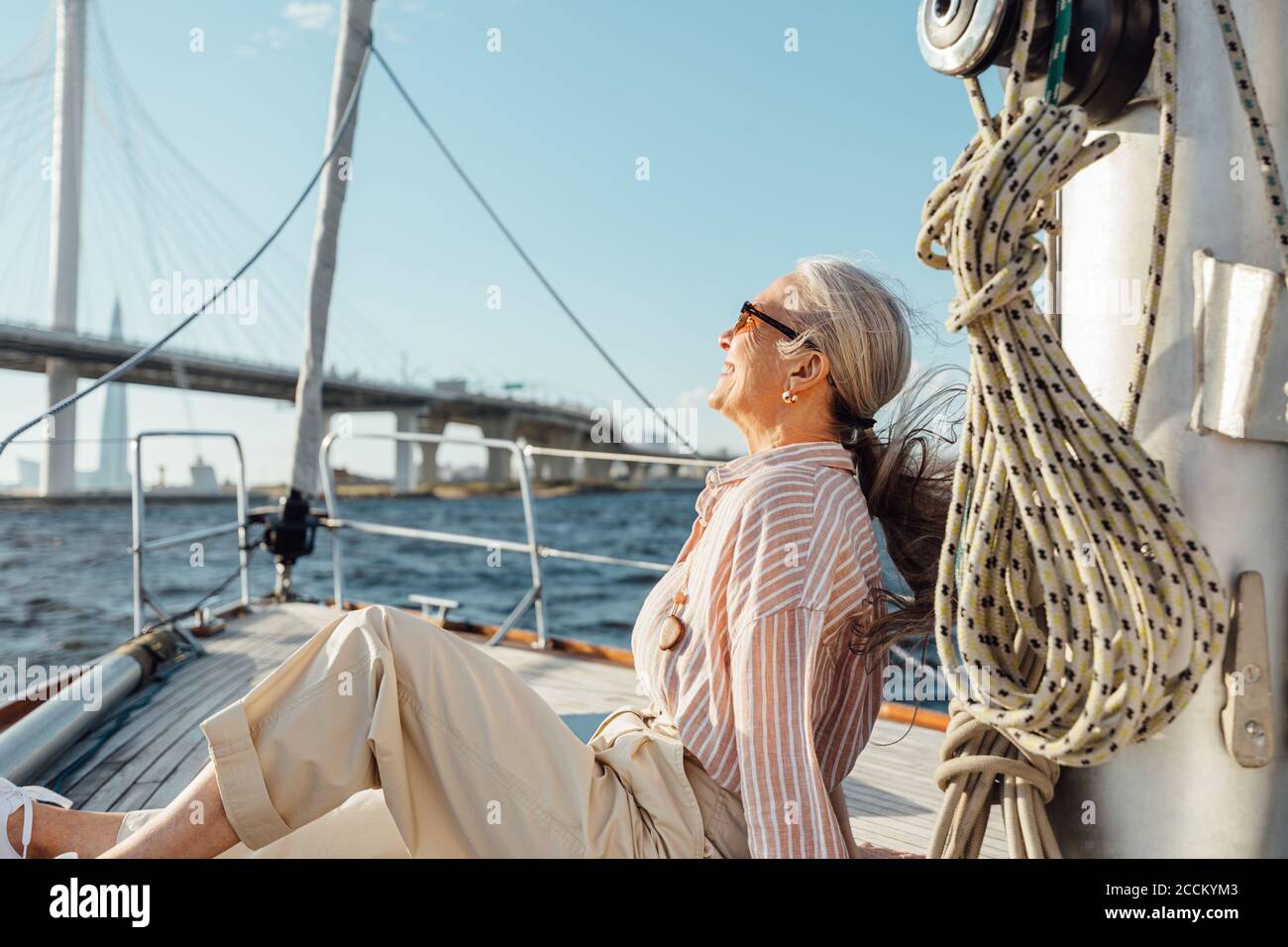 Vue latérale d'une femme mûre assise sur un yacht et profitant de la journée ensoleillée. Femme sénior se détendant sur un bateau privé. Banque D'Images