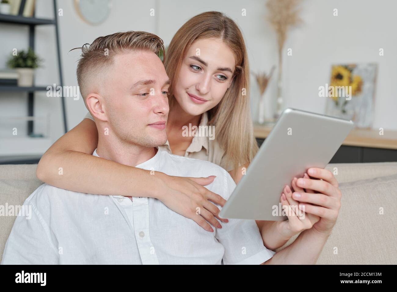 Blonde jeune jolie femme embrassant mari et lui montrant en ligne biens Banque D'Images