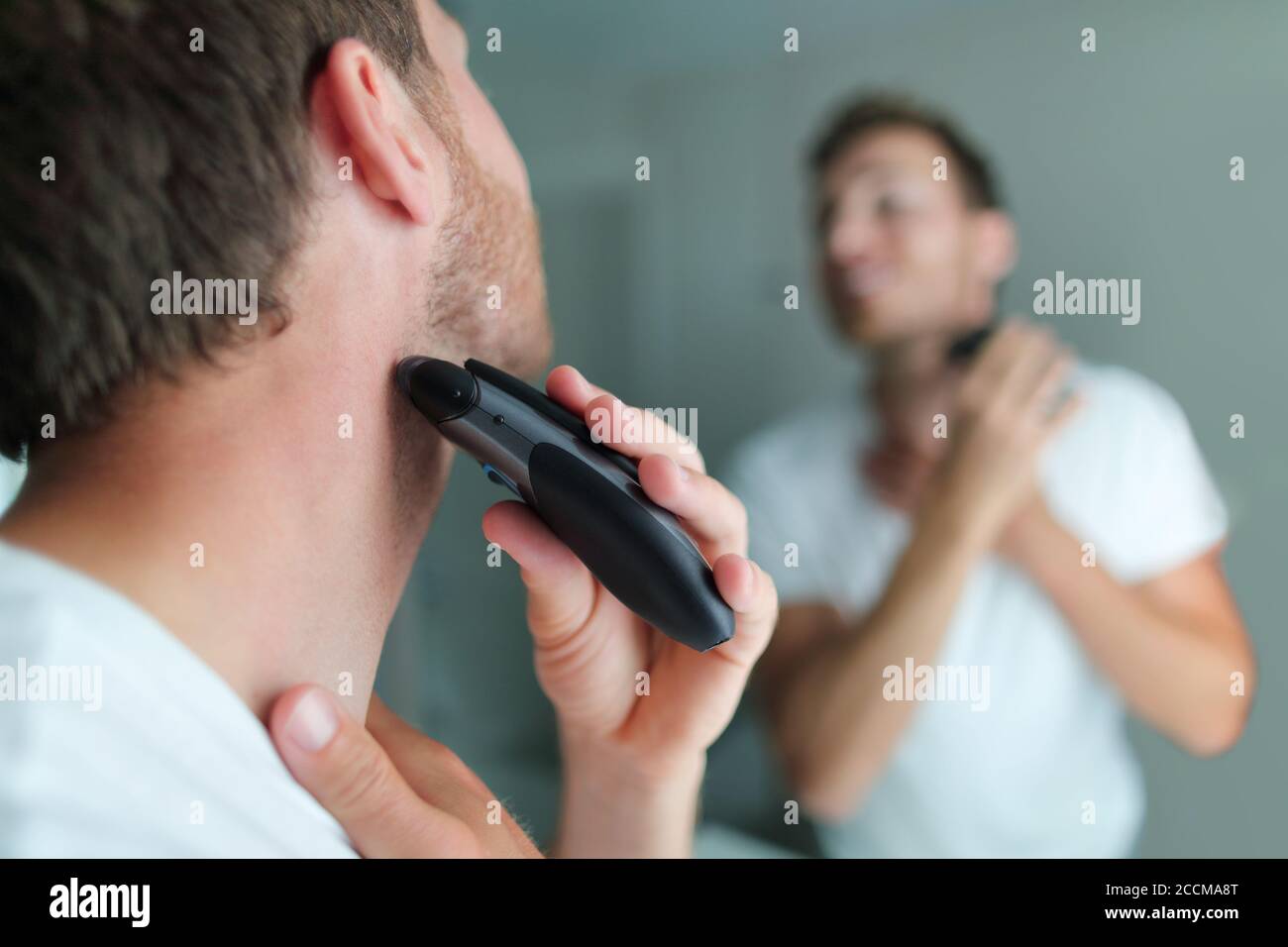 Homme se raser la barbe à l'aide d'un rasoir électrique. Concept de soins de beauté pour hommes. Maison style de vie jeune personne regardant la salle de bains miroir de tonte des cheveux Banque D'Images