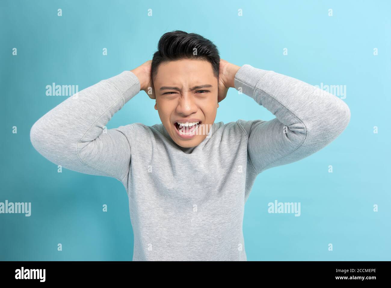 Stress émotionnel. Un jeune homme frustré tient les mains sur les oreilles tout en se tenant contre un fond bleu Banque D'Images