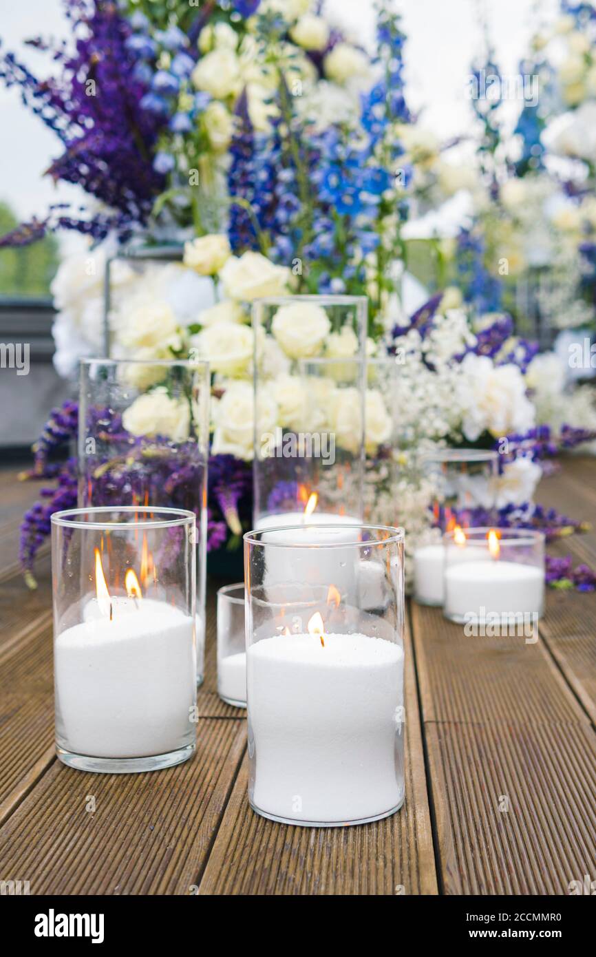 Gros plan de bougies blanches à la réception de mariage avec fleurs blanches, blu et violettes, à l'extérieur. Décoration de mariage élégante et luxueuse lors de la cérémonie Banque D'Images