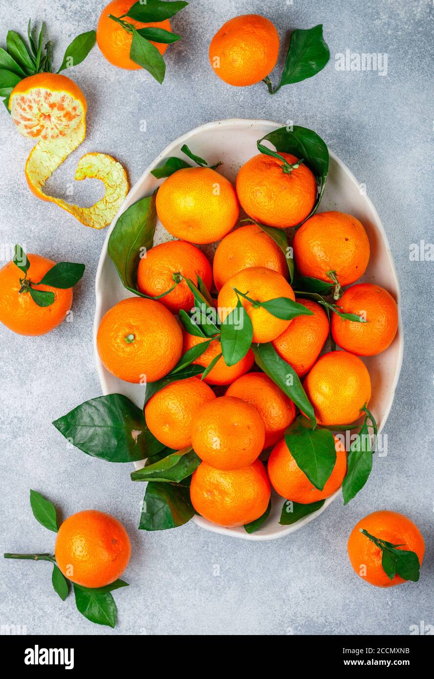 Agrumes frais mandarine orange fruit (mandarines, clémentines) avec des feuilles dans un plat léger sur fond de pierre grise ou de béton. Mise au point sélective, à Banque D'Images