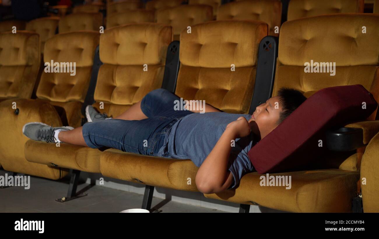 Un garçon allongé sur un fauteuil au cinéma. Banque D'Images