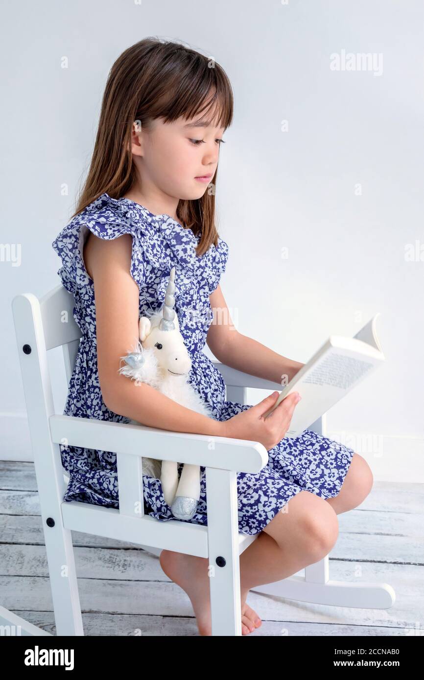 Douce fille de 7 ans lisant un livre sur un fauteuil à bascule Banque D'Images