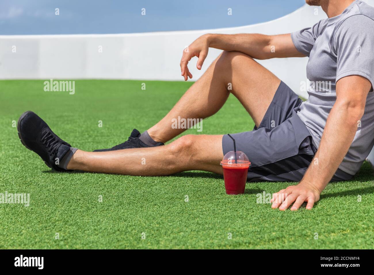 Juice smoothie sport homme se détendant apprécier après l'entraînement petit déjeuner matin assis sur l'herbe extérieure à la maison ou salle de fitness. Athlète buvant des fruits rouges Banque D'Images