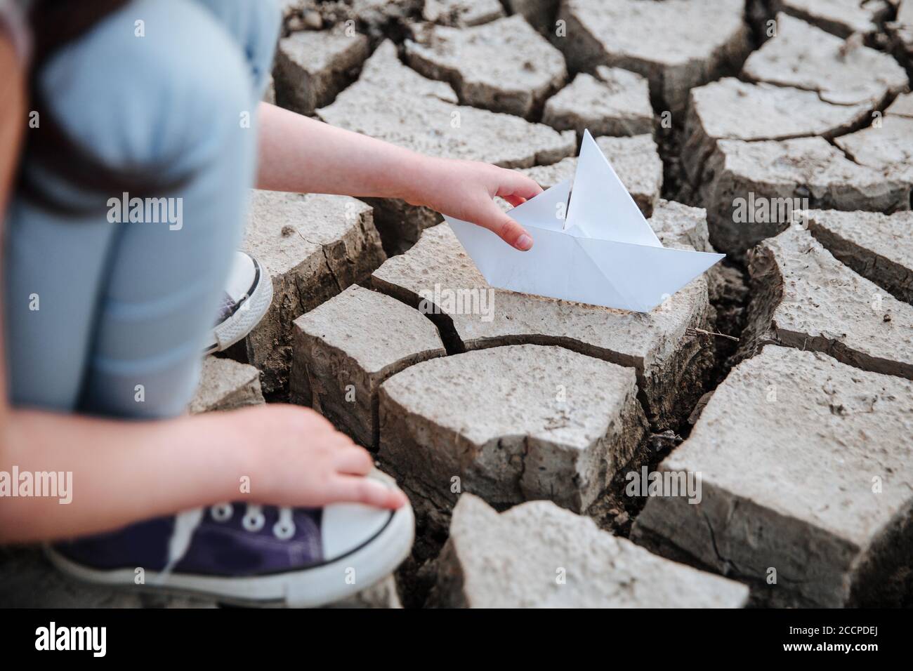 La fille abaisse le bateau en papier sur le sol sec et fissuré. Crise de l'eau et changement climatique concept. Réchauffement de la planète Banque D'Images