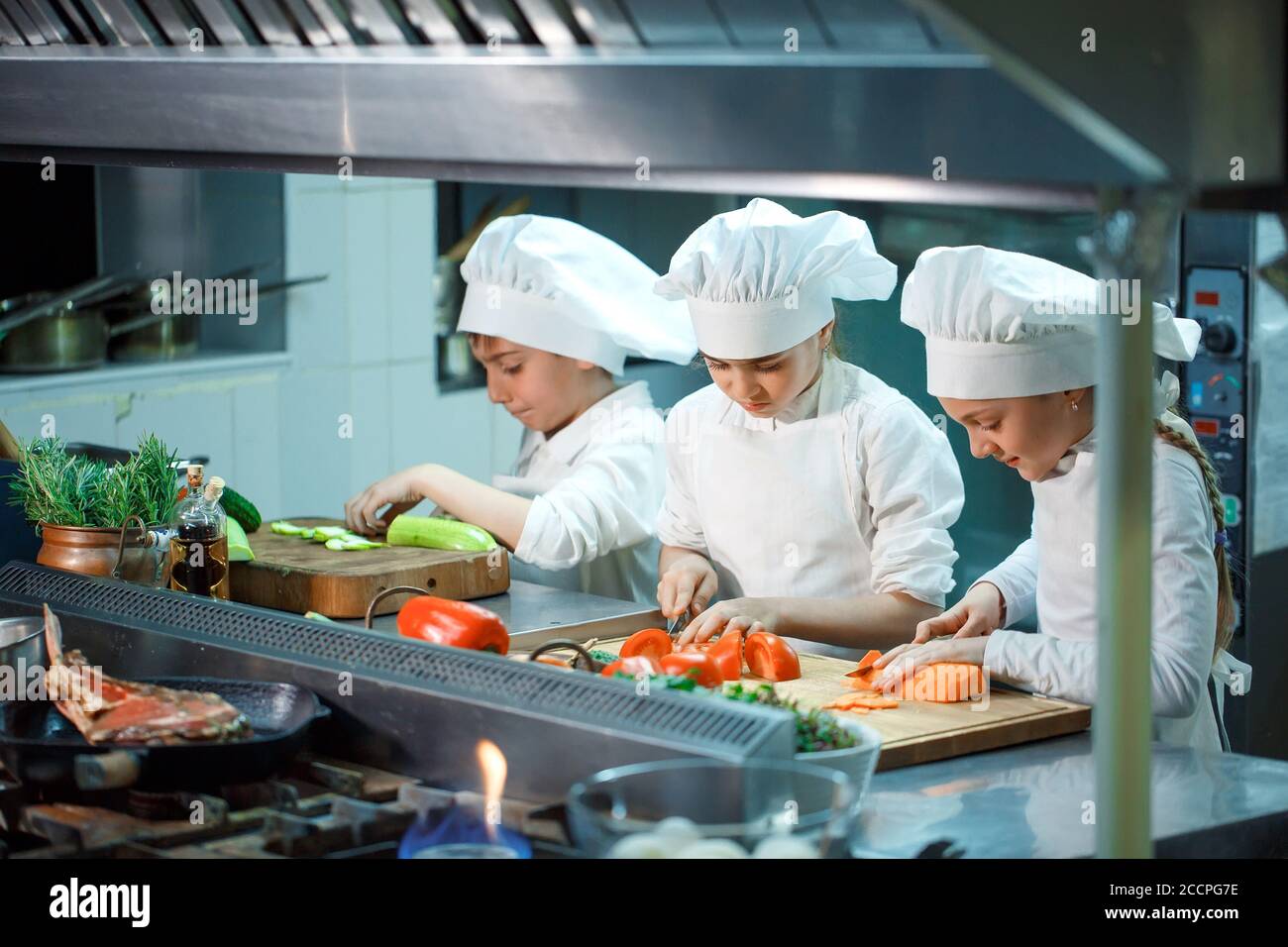 Les enfants meulent les légumes dans la cuisine d'un restaurant. Banque D'Images