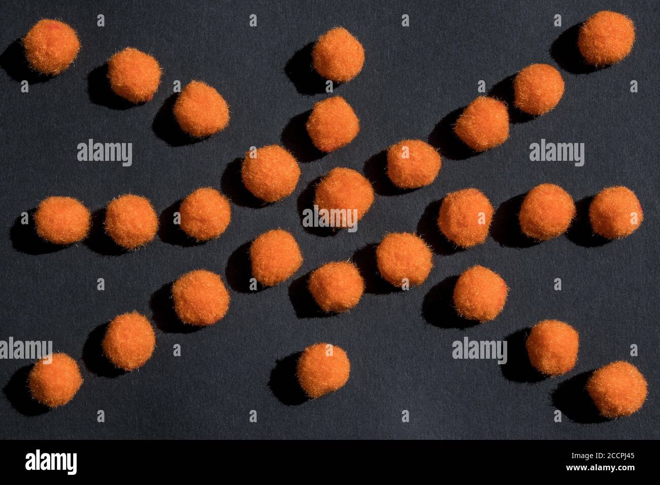 Arrière-plan de fête d'Halloween. Les pompons orange moelleux sont en forme d'araignée sur fond noir. Lumière vive et ombre. Vue de dessus, plan d'appartement. Banque D'Images
