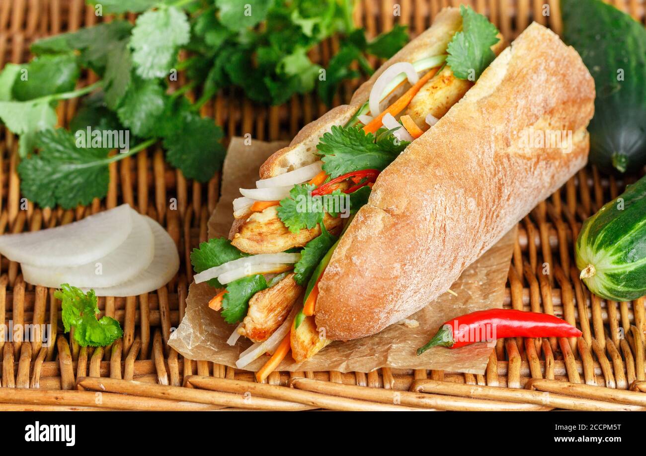 Sandwich à la baguette avec poulet frit et légumes frais - carottes, concombre, daikon, poivron rouge et coriandre (coriandre) sur une table en osier. Délicieux Banque D'Images