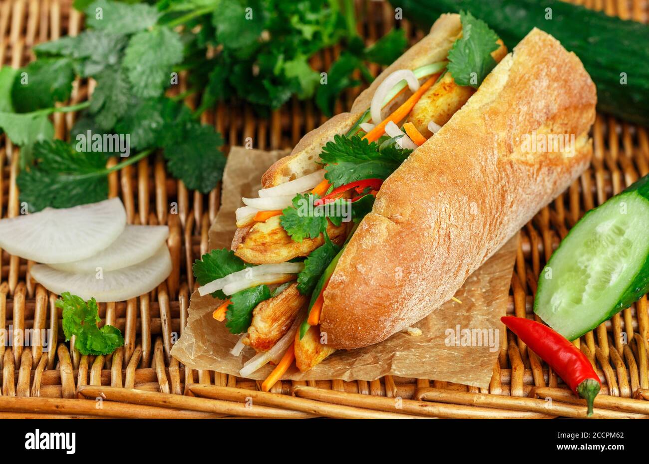 Sandwich à la baguette avec poulet frit et légumes frais - carottes, concombre, daikon, poivron rouge et coriandre (coriandre) sur une table en osier. Délicieux Banque D'Images