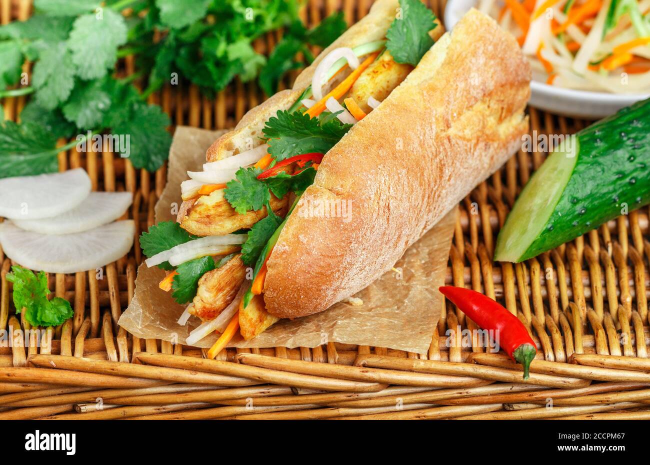 Sandwich à la baguette avec poulet frit et légumes frais - carottes, concombre, daikon, poivron rouge et coriandre (coriandre) sur une table en osier. Délicieux Banque D'Images