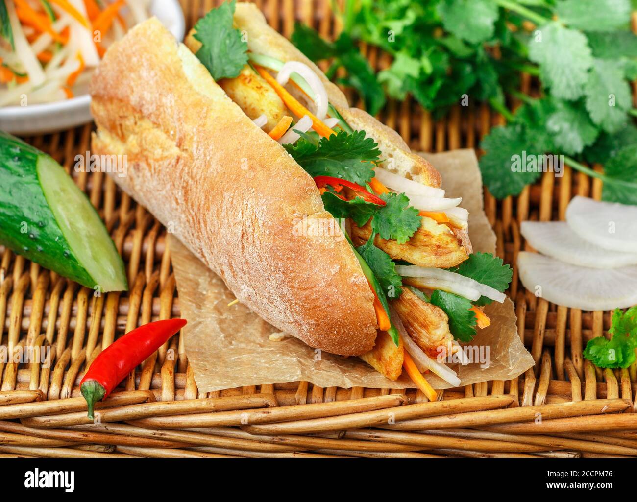 Sandwich à la baguette avec poulet frit et légumes frais - carottes, concombre, daikon, poivron rouge et coriandre (coriandre) sur une table en osier. Délicieux Banque D'Images