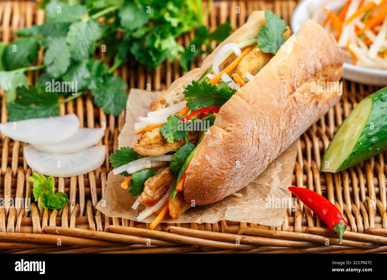 Sandwich à la baguette avec poulet frit et légumes frais - carottes, concombre, daikon, poivron rouge et coriandre (coriandre) sur une table en osier. Délicieux Banque D'Images