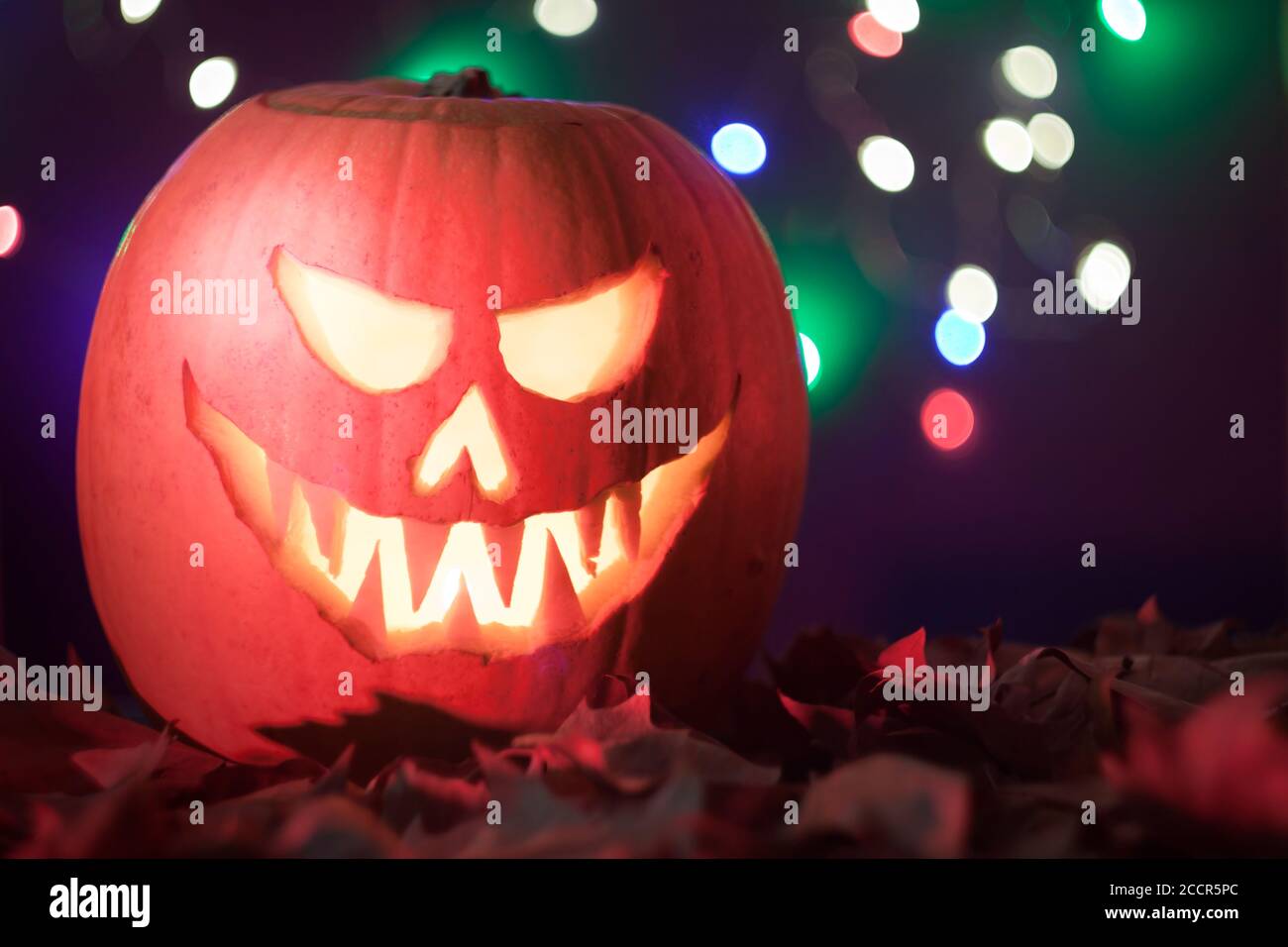 Jack O'Lantern illuminé effrayant halloween citrouille sculptée sur fond bokeh sombre avec espace de copie. Banque D'Images