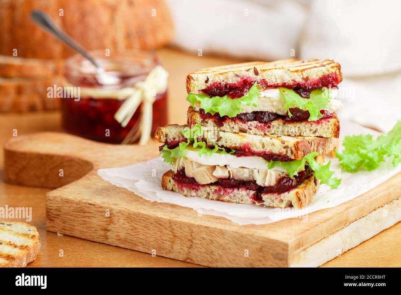 Délicieux sandwich à la dinde ou au poulet avec du fromage brie ou Camembert, de la laitue et du chutney aux canneberges (lingonberry, cowberry) sur du pain aux céréales avec du lin See Banque D'Images