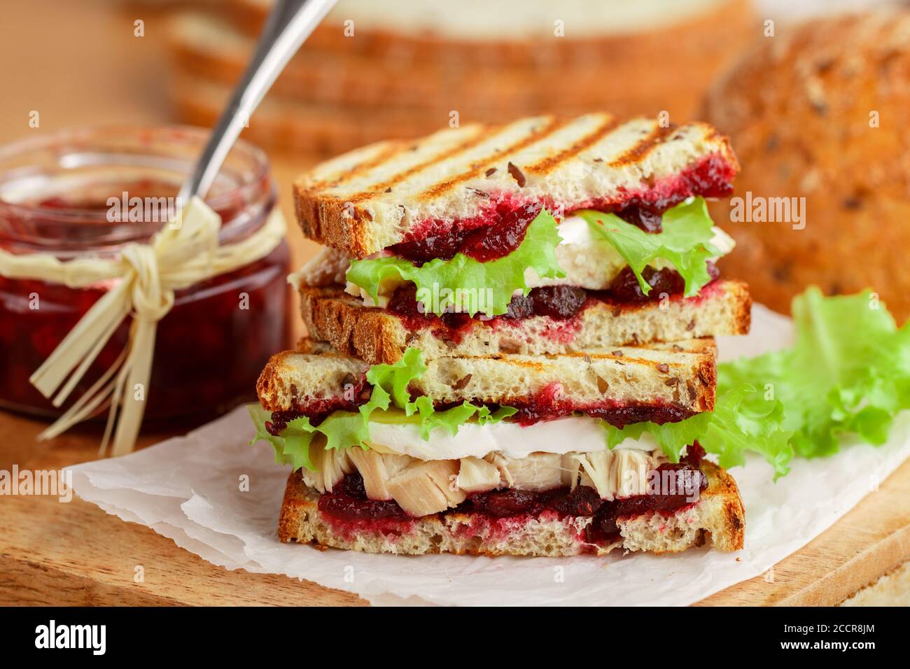 Délicieux sandwich à la dinde ou au poulet avec du fromage brie ou Camembert, de la laitue et du chutney aux canneberges (lingonberry, cowberry) sur du pain aux céréales avec du lin See Banque D'Images