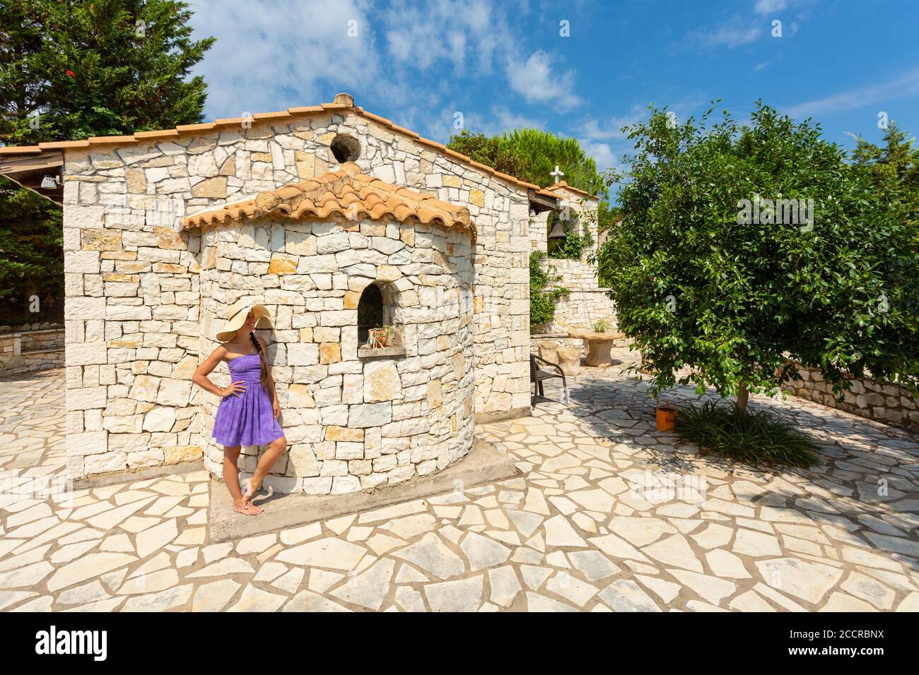 Une fille debout à côté d'une petite église grecque orthodoxe en pierre à Meganissi, Iles Ioniennes, Grèce Banque D'Images