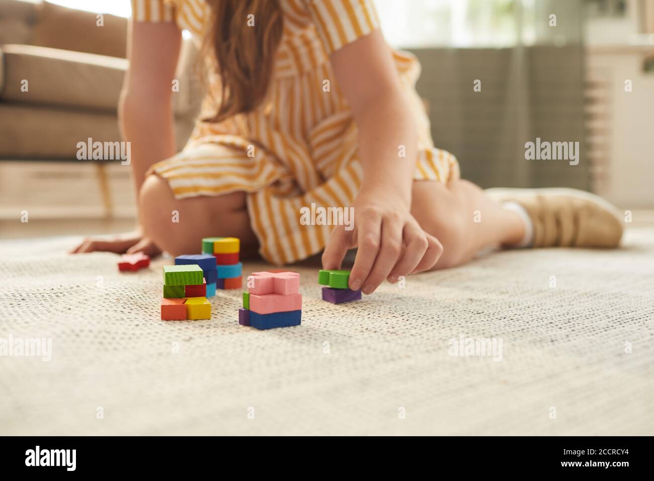 Une petite fille non reconnaissable qui joue avec des blocs colorés dans un espace intérieur chaleureux Banque D'Images