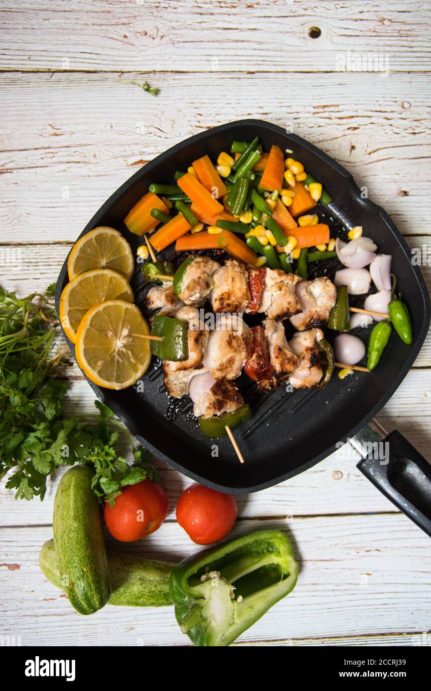 Vue de dessus des kebabs de poulet sur une casserole noire avec légumes et condiments Banque D'Images