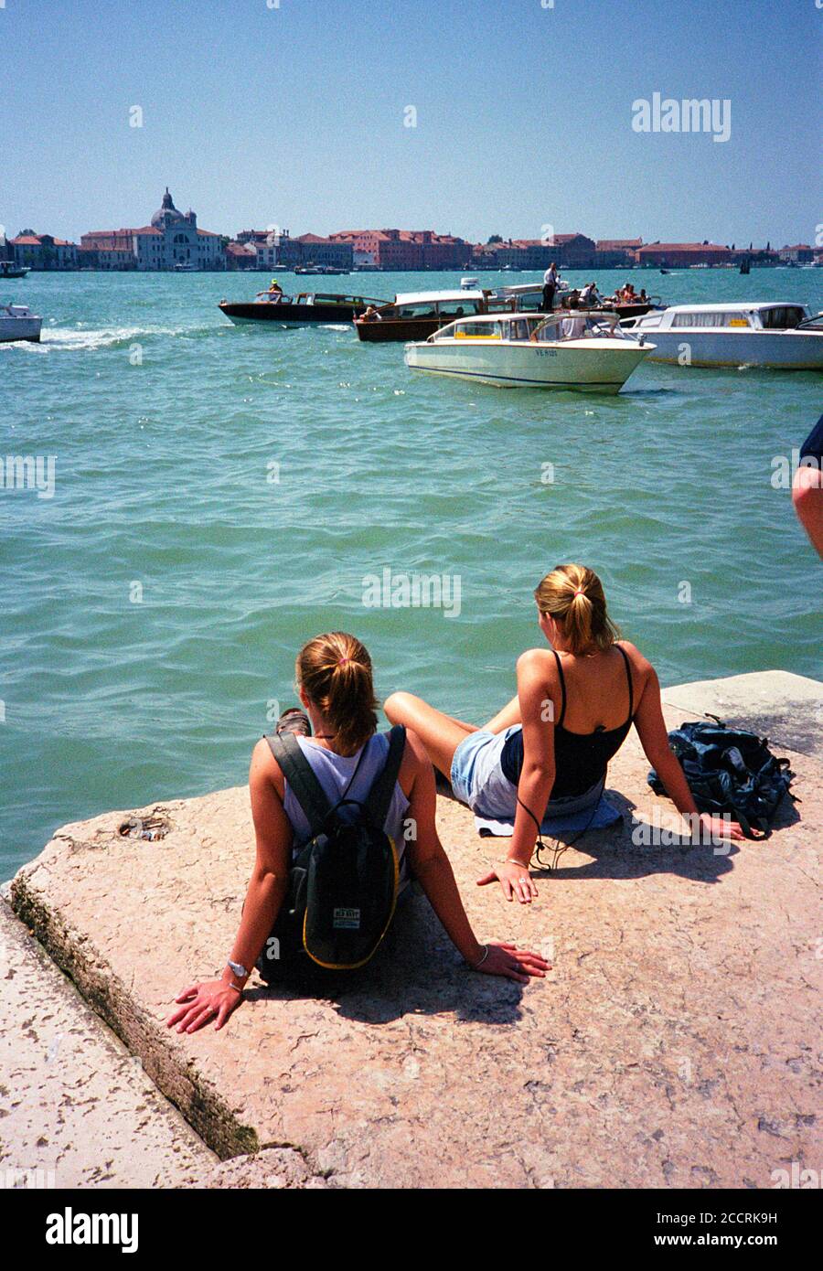 Deux touristes à Venise se détendant au soleil surplombant l'eau à la basilique di Santa d'un endroit derrière la Piazza San Marco. Banque D'Images