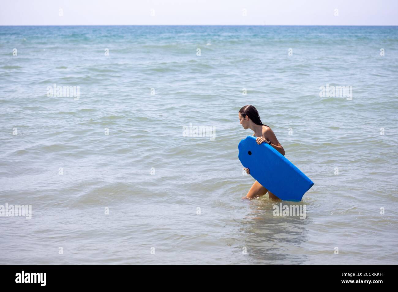 Une fille portant un bodyboard bleu sur la plage à commencez à surfer Banque D'Images