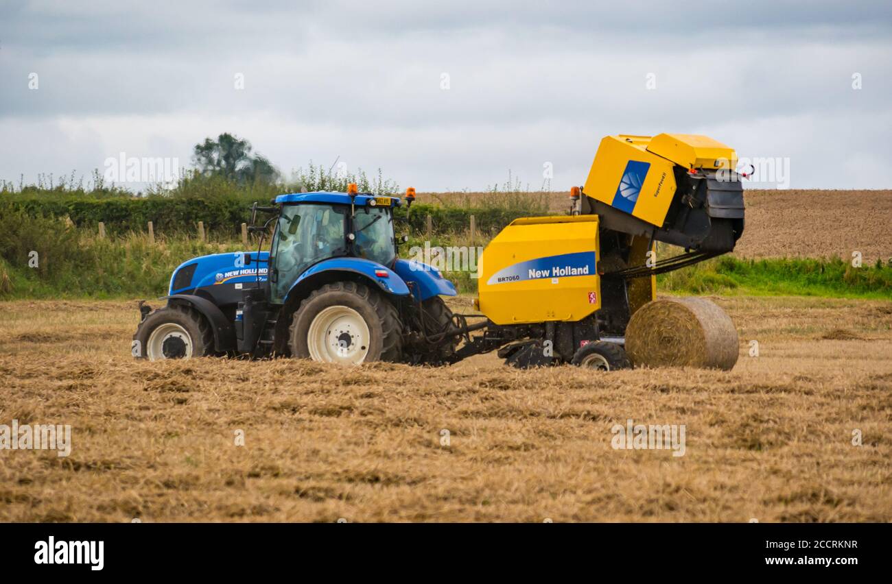Travailleur agricole conduisant le tracto avec une presse à foin dans le champ de récolte, East Lothian, Écosse, Royaume-Uni Banque D'Images