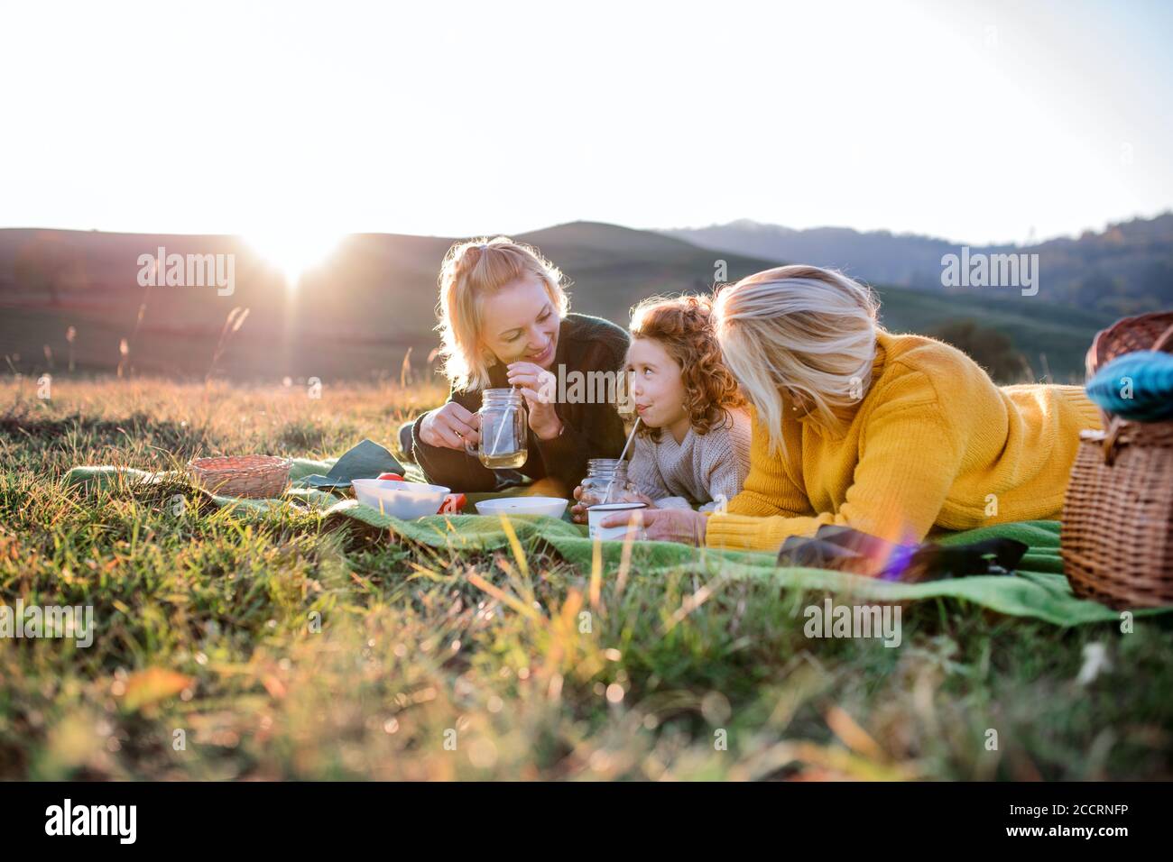 Petite fille avec mère et grand-mère ayant pique-nique dans la nature au coucher du soleil. Banque D'Images