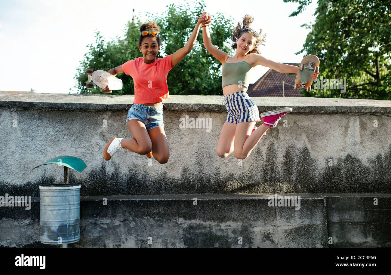 Jeunes adolescentes amies avec des planches à roulettes en plein air en ville, sautant. Banque D'Images