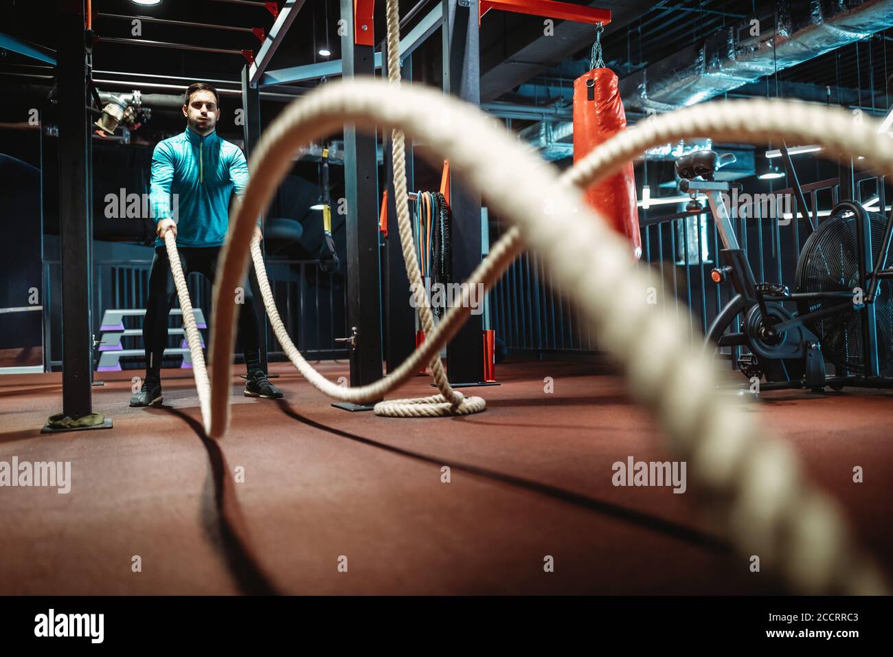 Homme de fitness s'entraîner avec des cordes de combat à la salle de gym. Banque D'Images