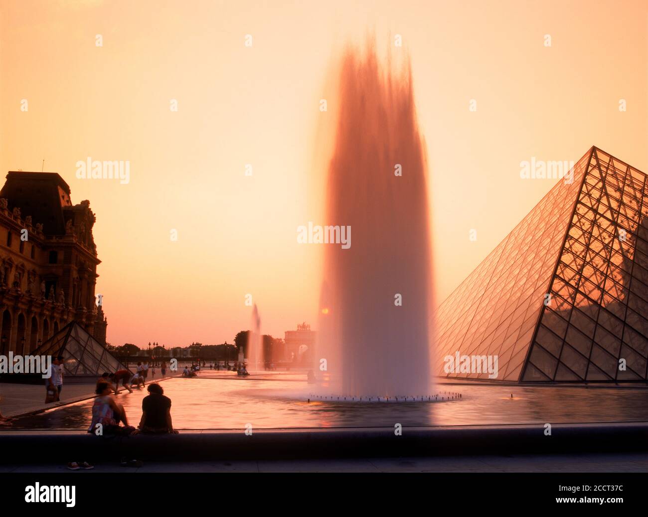 Personnes assises à la fontaine du musée du Louvre à Paris silhoueté dans la lumière du coucher du soleil Banque D'Images