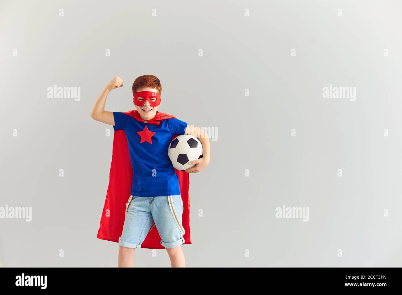 Garçon souriant en costume de super-héros montrant la puissance et tenant le ballon de football en main, espace de copie Banque D'Images