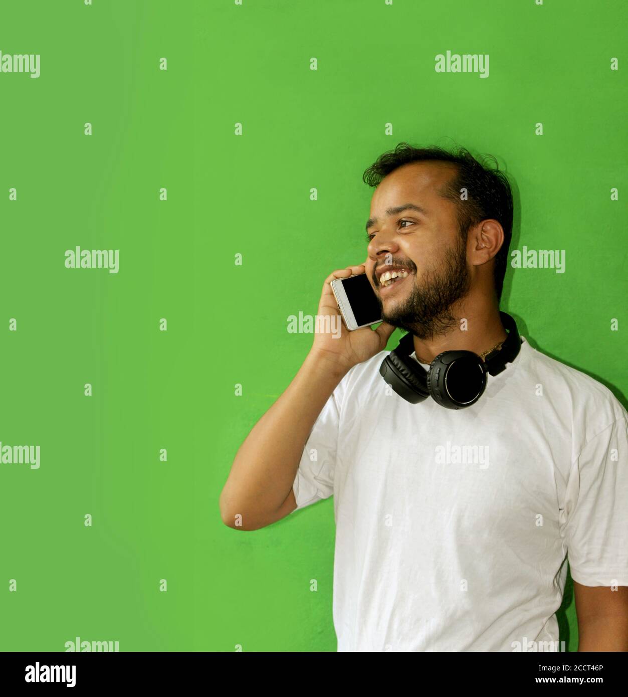 jeune homme souriant et souriant, parlant au téléphone et tenant un casque, jeune homme confiant portrait avec espace de texte sur fond vert, se Banque D'Images