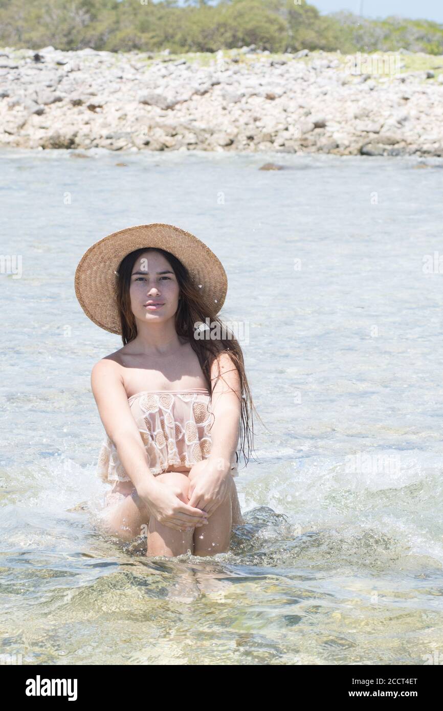 Charmante femme de race blanche sur un maillot de bain nu et un chapeau de plage Assis sur des rochers à l'île des caraïbes Los Roques venezuela Banque D'Images