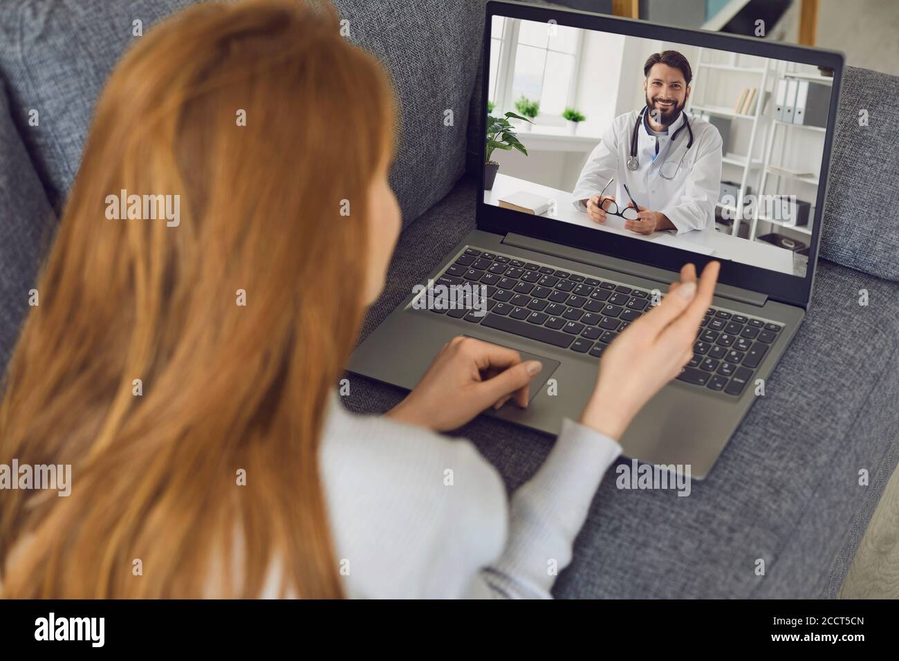 La femme se trouve sur le canapé à la maison et utilise un ordinateur portable pour appeler un médecin en ligne. Banque D'Images