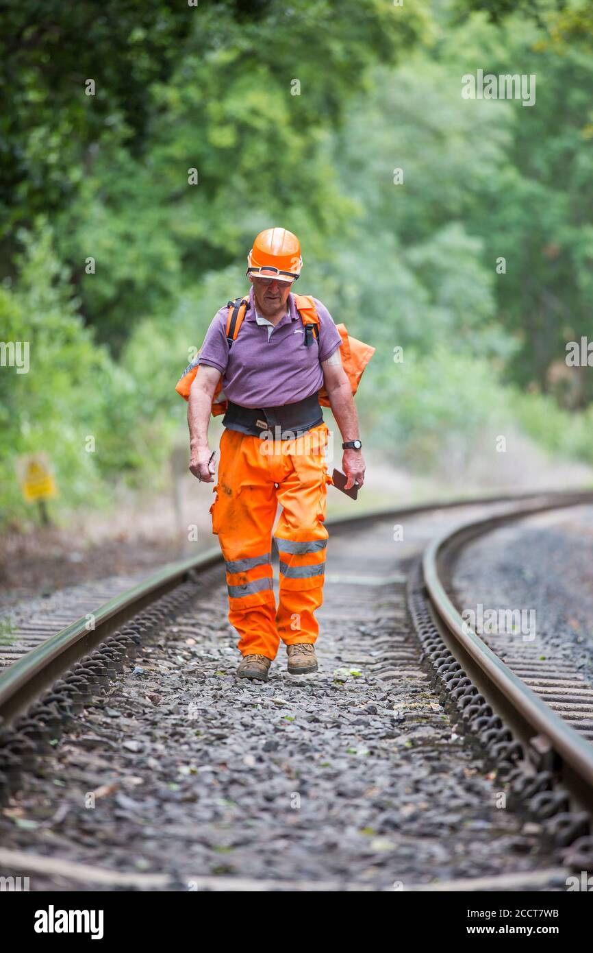 Travailleur ferroviaire, à l'avant, à pied isolé le long de la ligne de chemin de fer du patrimoine britannique, inspectant la voie pour les dommages. Entretien courant des chemins de fer, inspection. Banque D'Images