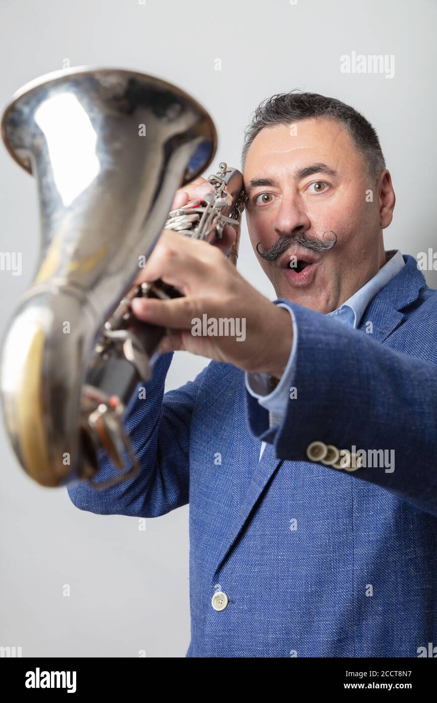 Un homme, sombre, à cheveux courts, une longue moustache sur son épaule, tient une clarinette basse. Look surpris Studio, fond clair. Photo de haute qualité Banque D'Images