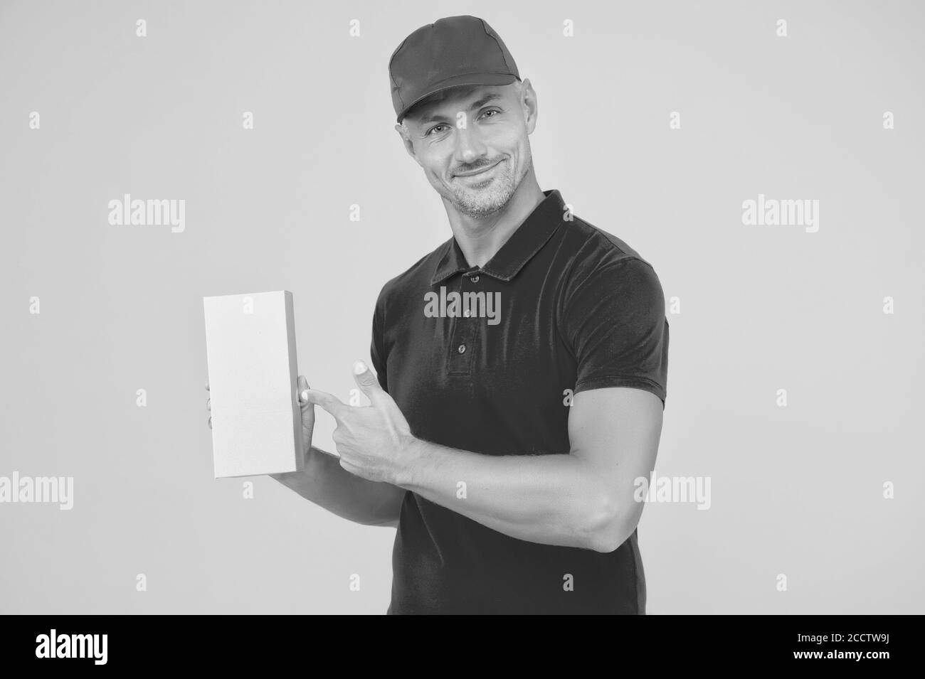 Votre colis notre passion. Un préposé à la messagerie pointe le doigt sur la boîte à colis. Liveur sur fond jaune uniforme rouge. Service de livraison de colis. Poste de colis. Tout à votre porte, espace de copie. Banque D'Images