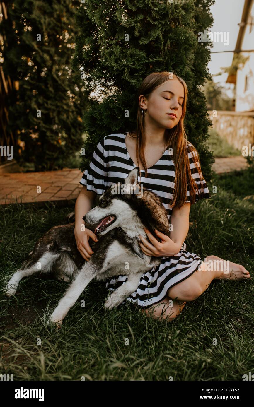 blonde fille est assis sur l'herbe verte avec un chien husky aux yeux bleus Banque D'Images