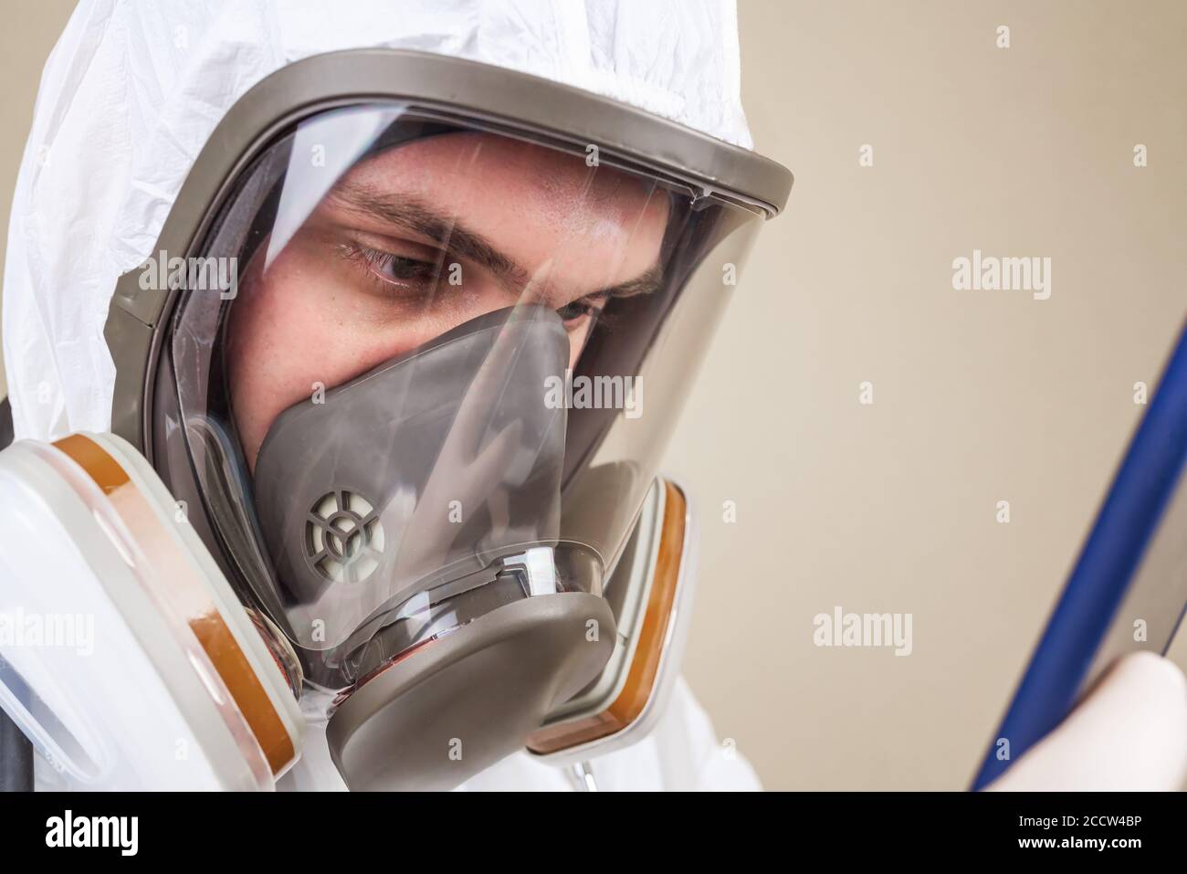 Médecin en costume médical de protection et masque respiratoire intégral regardez son téléphone portable à la main isolé Banque D'Images