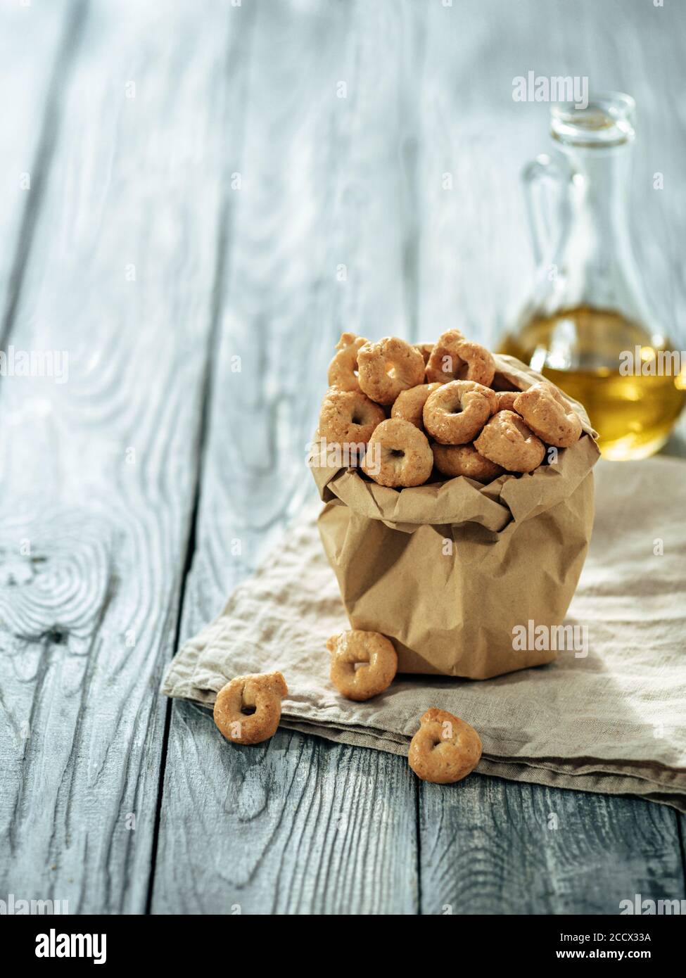 Taralli ou taralini italien traditionnel dans un sac en papier sur une ancienne table en bois grise. Photo rustique de taralli apéritif avec espace copie. Verticale Banque D'Images