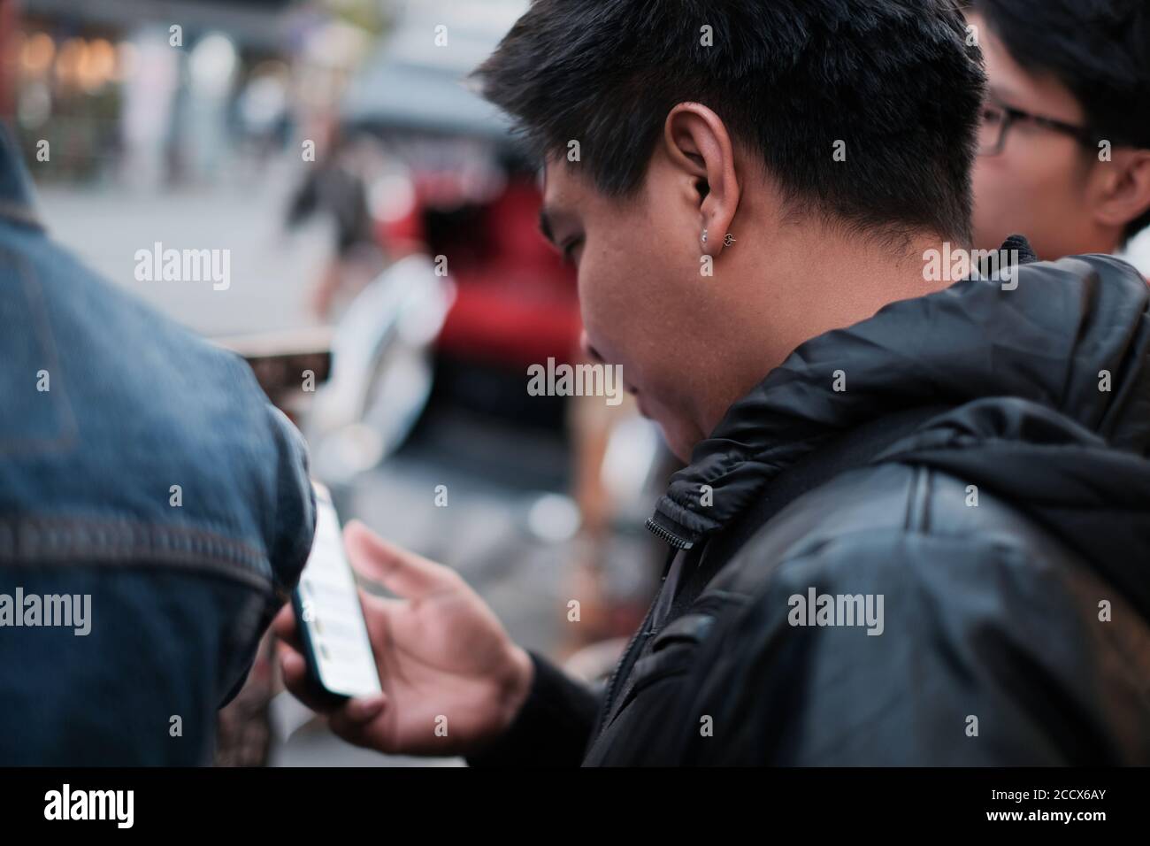 Gros plan jeune homme asiatique porte une capuche noire et un diamant ecouteurs lorsque vous utilisez un smartphone et que vous voyagez en ville avec des amis Banque D'Images