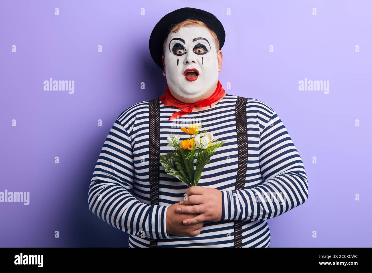 surpris jeune homme choqué avec visage peint, vêtements rayés et bretelles  avec large bouche ouverte tenant le bouquet de fleurs artificielles.isolé  bleu Photo Stock - Alamy
