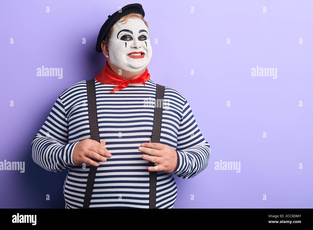 joyeux artiste mime avec sourire créning poignant , touchant ses bretelles regardant la caméra . comédie sketch.copy space. isolé arrière-plan bleu. Banque D'Images