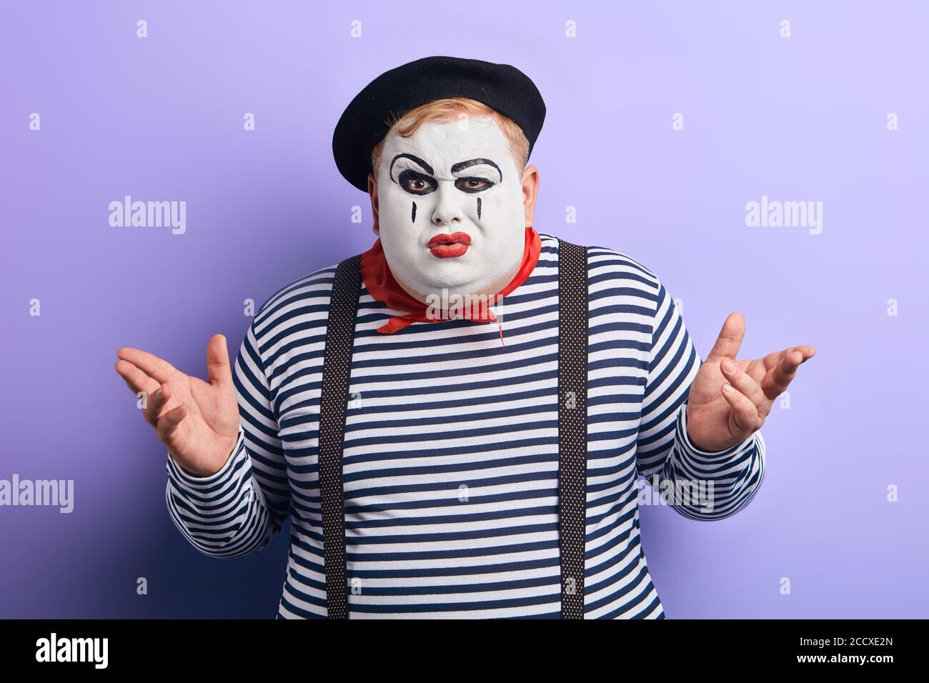 le clown perplexe ne sait pas ce qui s'est passé, ont le regard malheureux, le mime de colère grave avec les bras levés regardant la caméra . arrière-plan bleu isolé, stu Banque D'Images