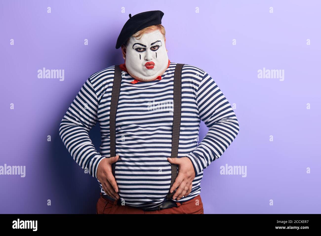 clown drôle avec les mains sur son ventre, prêtant ballon d'air. photo de gros plan. arrière-plan bleu isolé, prise en studio Banque D'Images