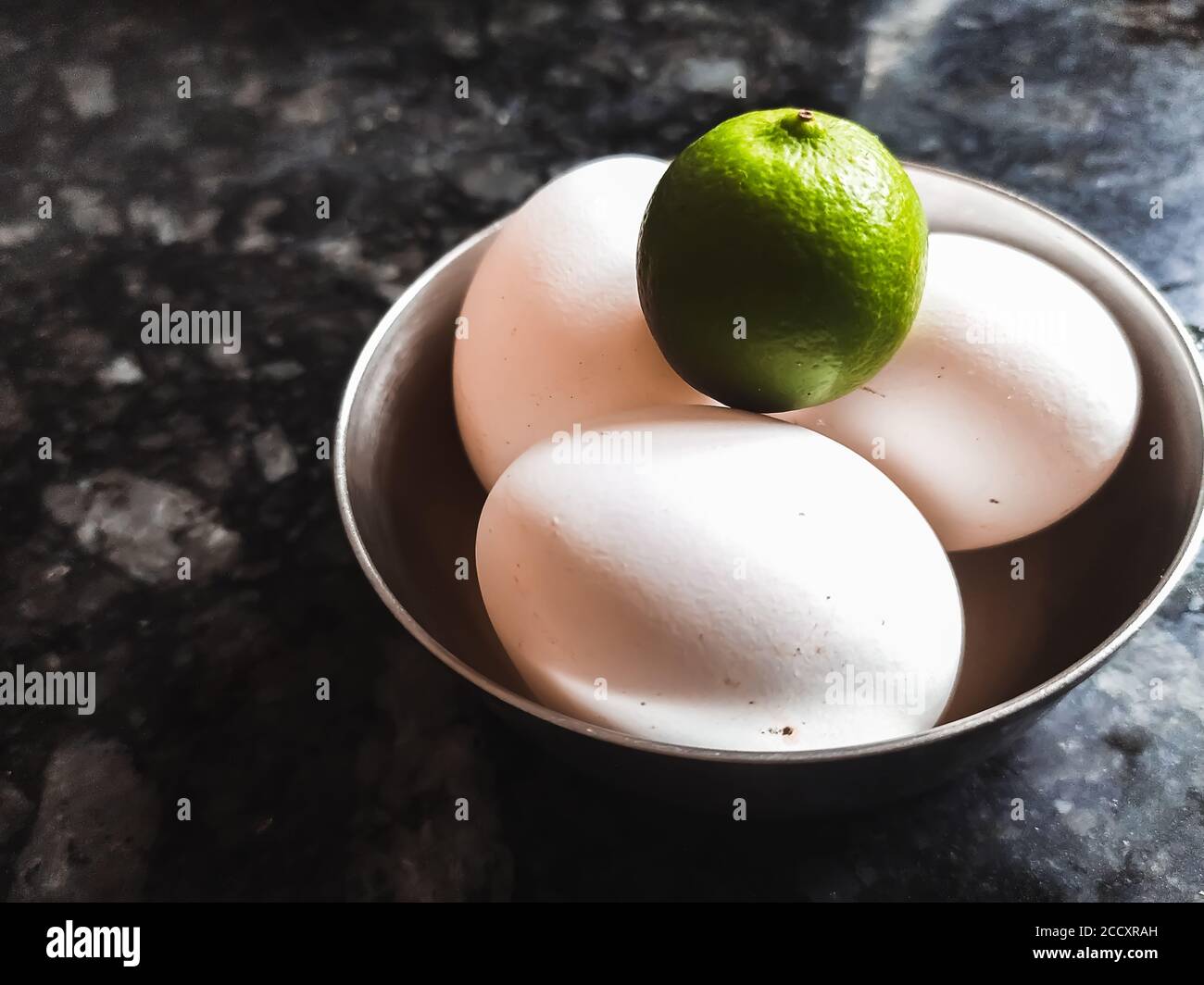 Le citron vert repose sur trois œufs de pâques sous un bol sur sol carrelé. Banque D'Images