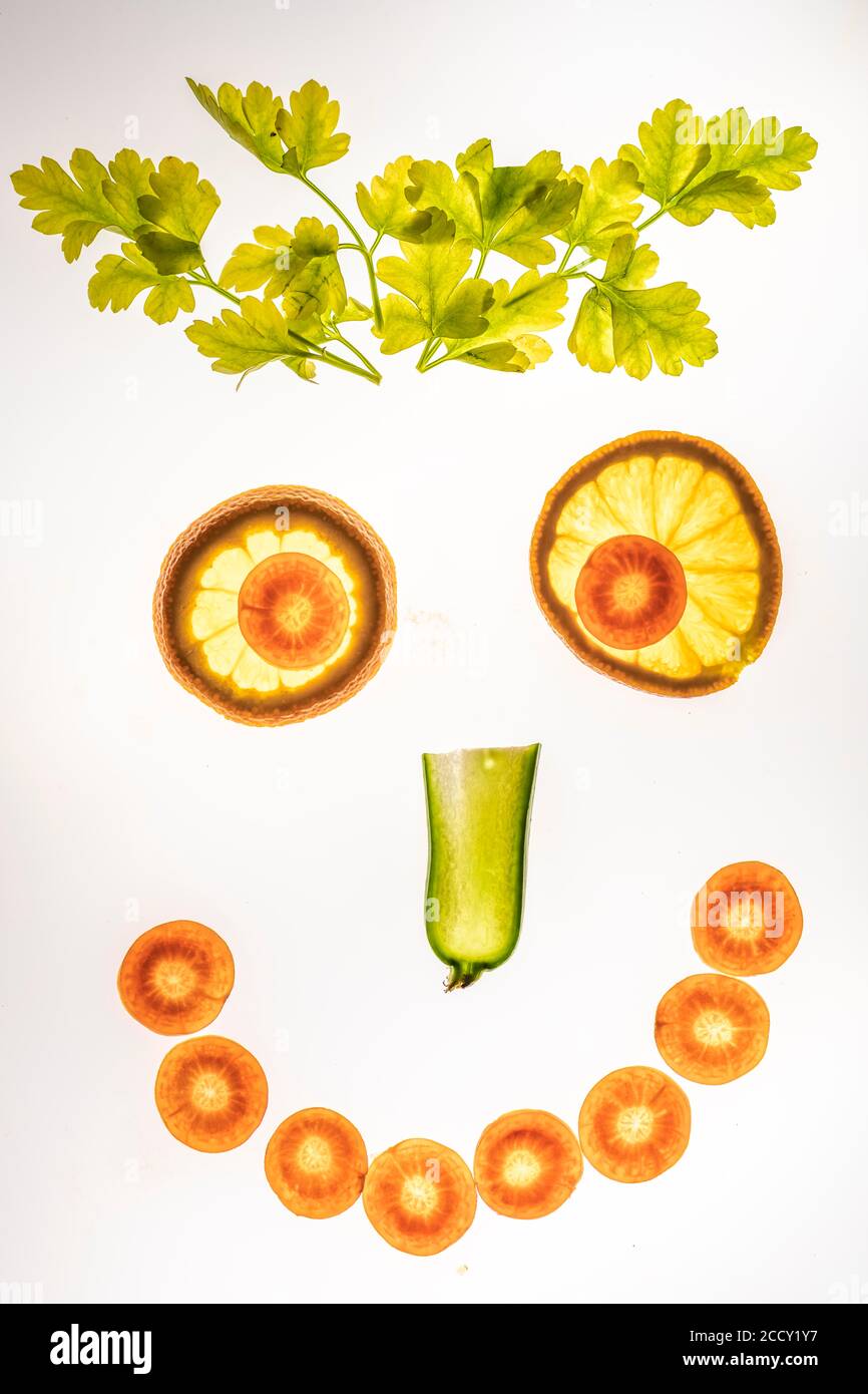 Visage riant de légumes et de fruits, visage souriant, tranches de concombre, carotte et orange avec persil, fond blanc, photographie alimentaire Banque D'Images