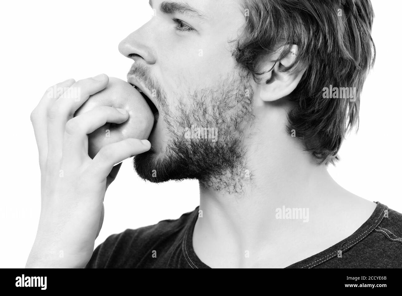 Un gars avec une barbe qui mord une pomme verte isolée sur fond blanc. Vue latérale, concept de nutrition saine Banque D'Images